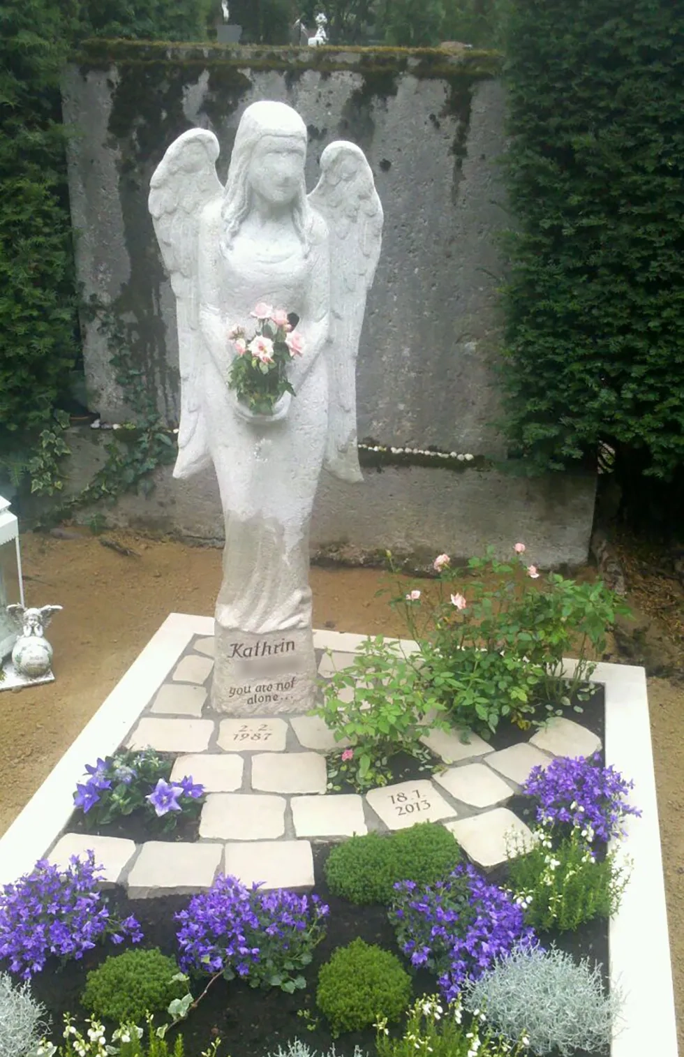 Grab mit grauer Engelsstatue und blauen Blumen